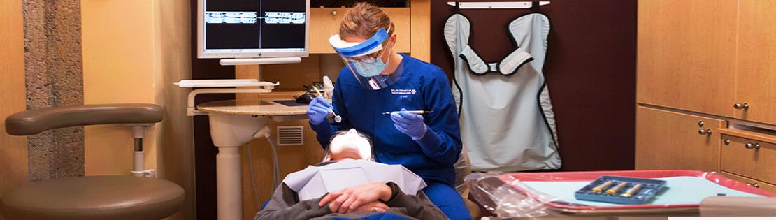 A dental student works on another person at a dental clinic